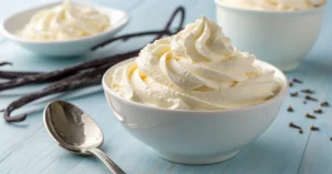 Fresh homemade whipped cream in a white bowl with a silver spoon on a light blue background, light and fluffy texture with va