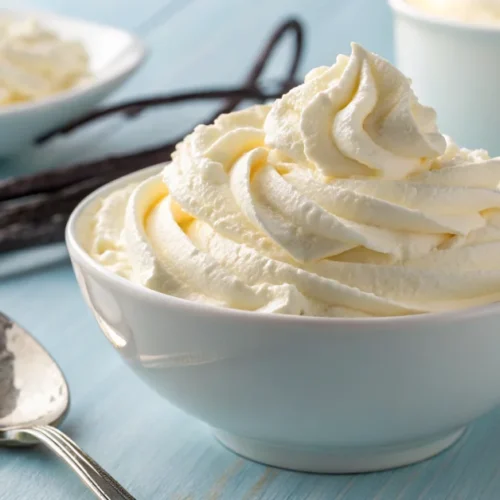 Fresh homemade whipped cream in a white bowl with a silver spoon on a light blue background, light and fluffy texture with va
